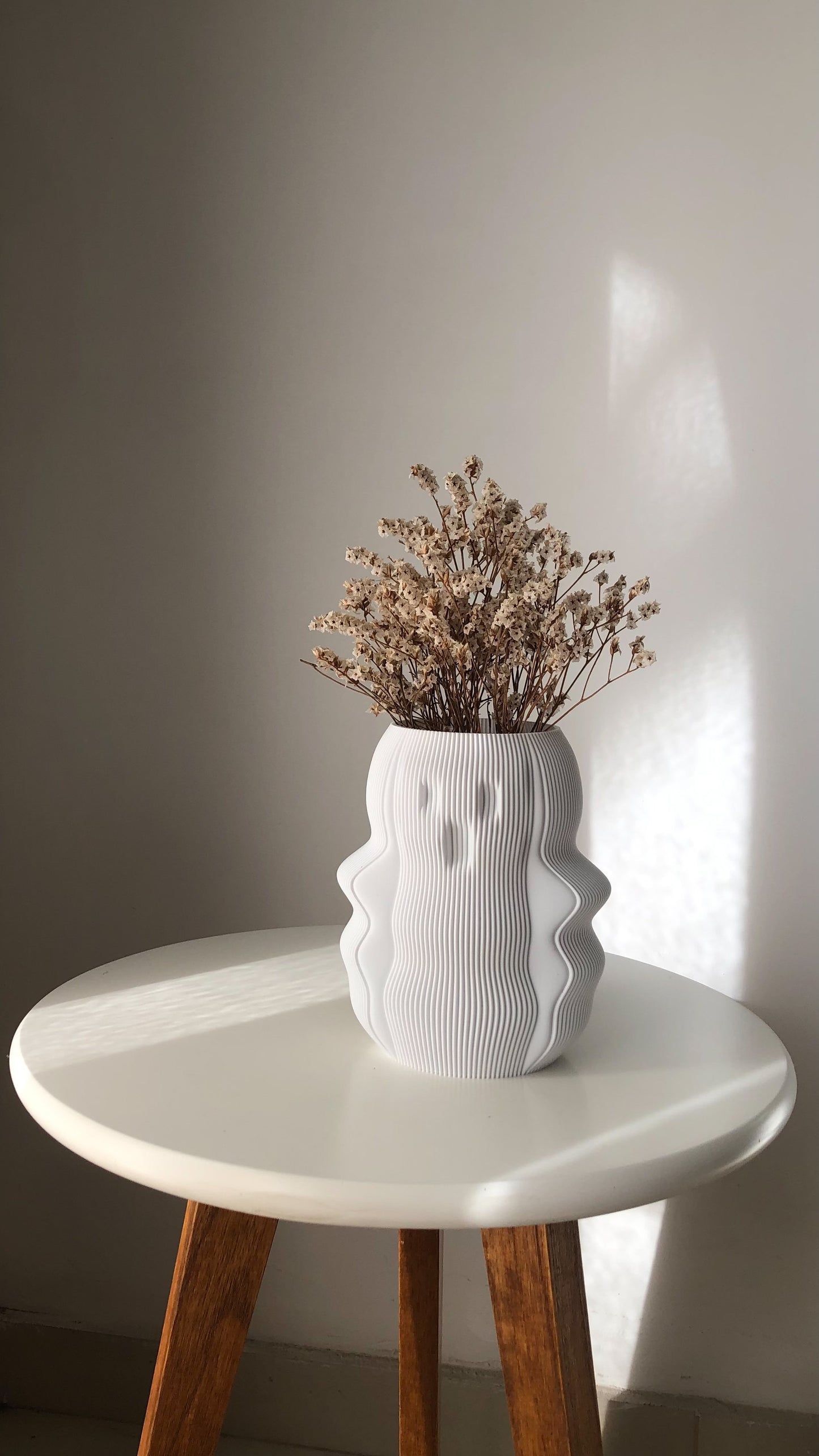 Unique white vase with a textured design, filled with dried flowers on a round table