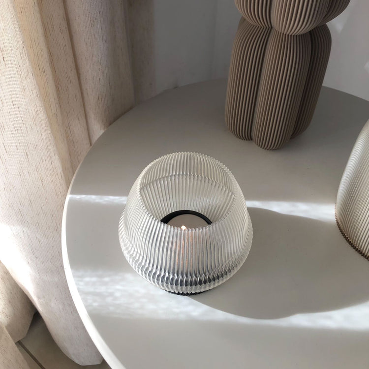 Translucent ribbed decorative tealight candle covers displayed on a modern round table with sculpted vases and soft sunlight