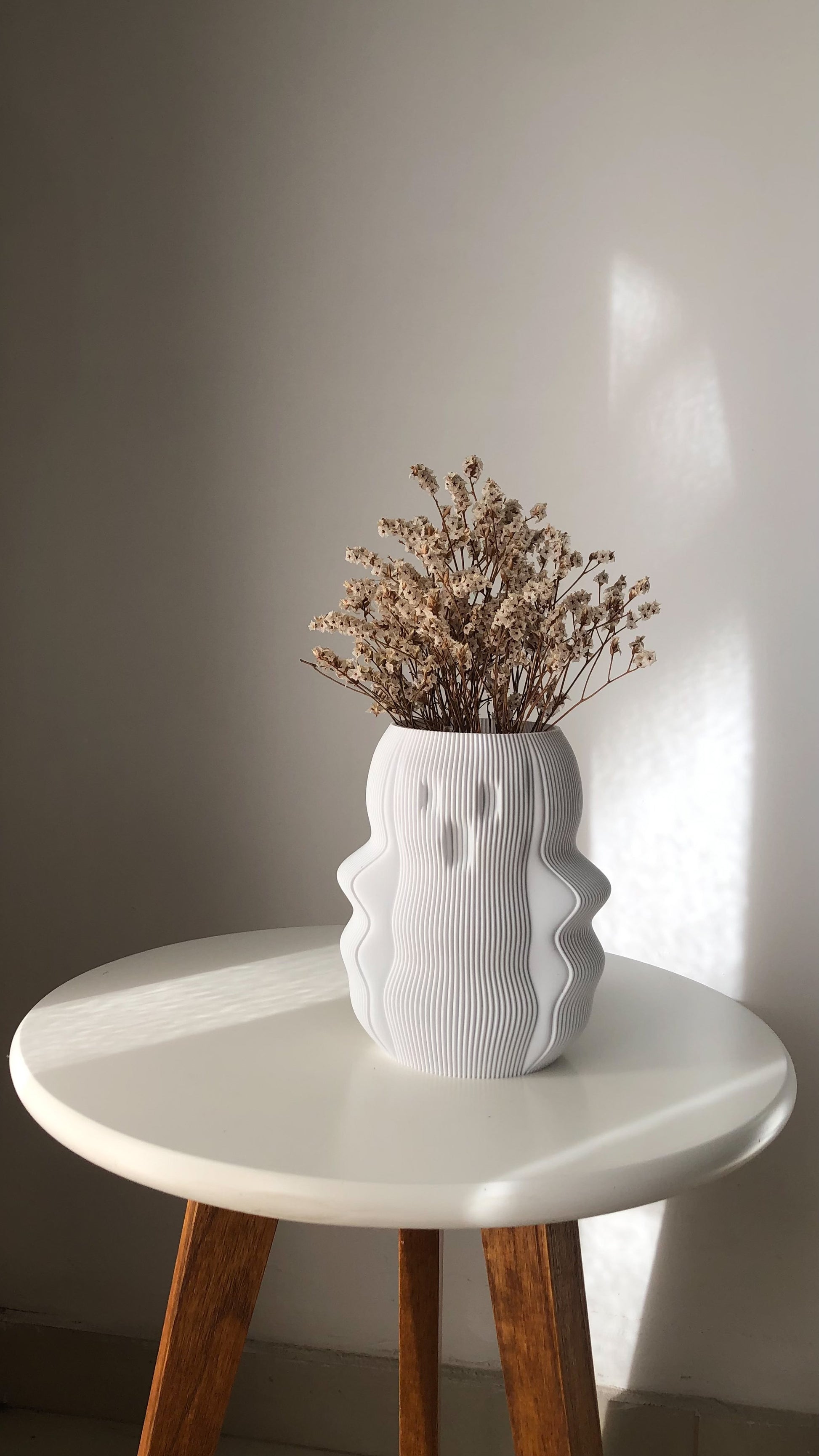 Unique white vase with a textured design, filled with dried flowers on a round table