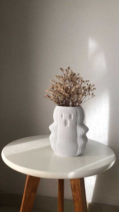 Unique white vase with a textured design, filled with dried flowers on a round table